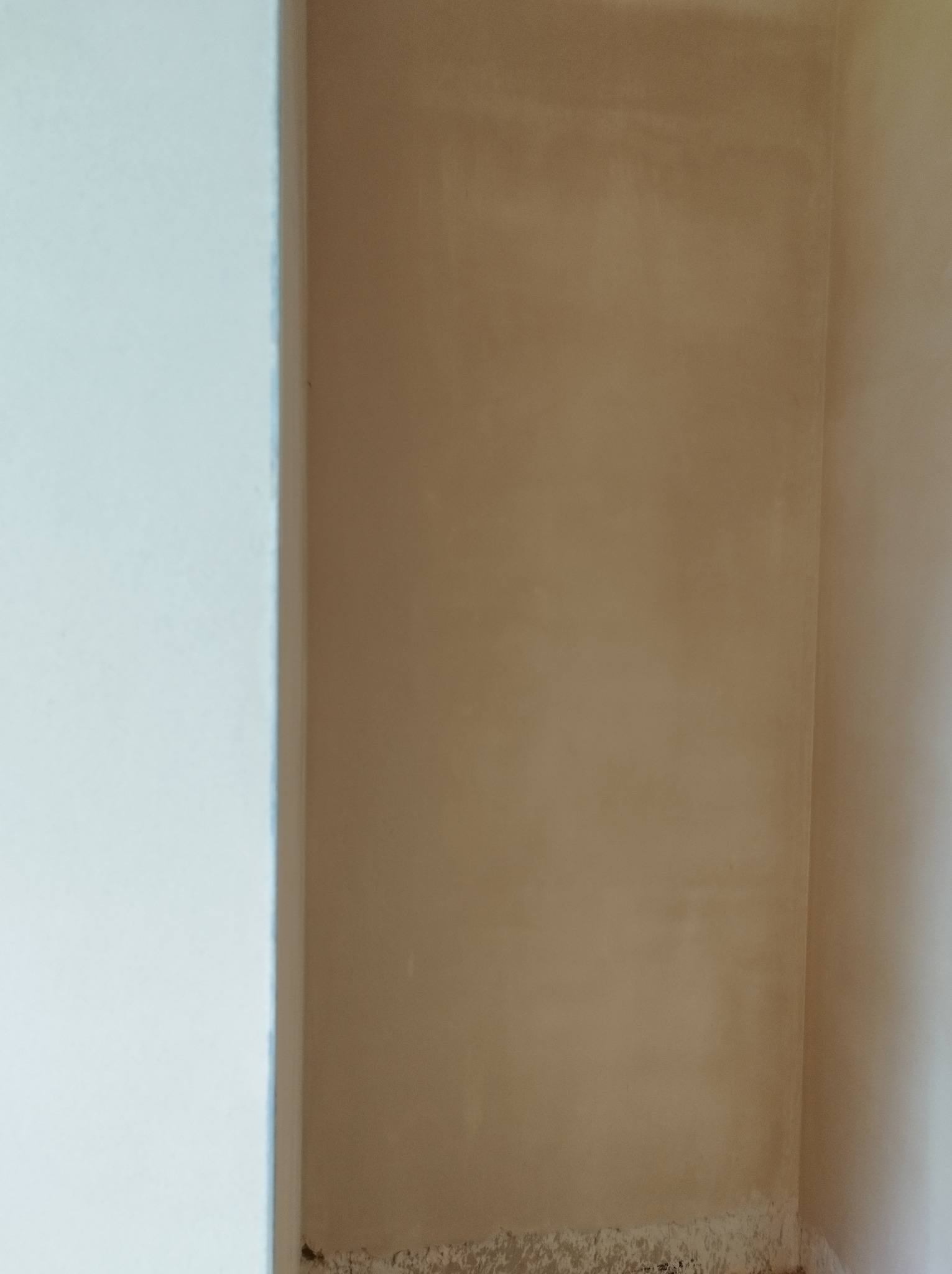 Świeżo nałożony tynk maszynowy w narożniku pomieszczenia, widoczne nierówności i resztki materiału u dołu ściany.