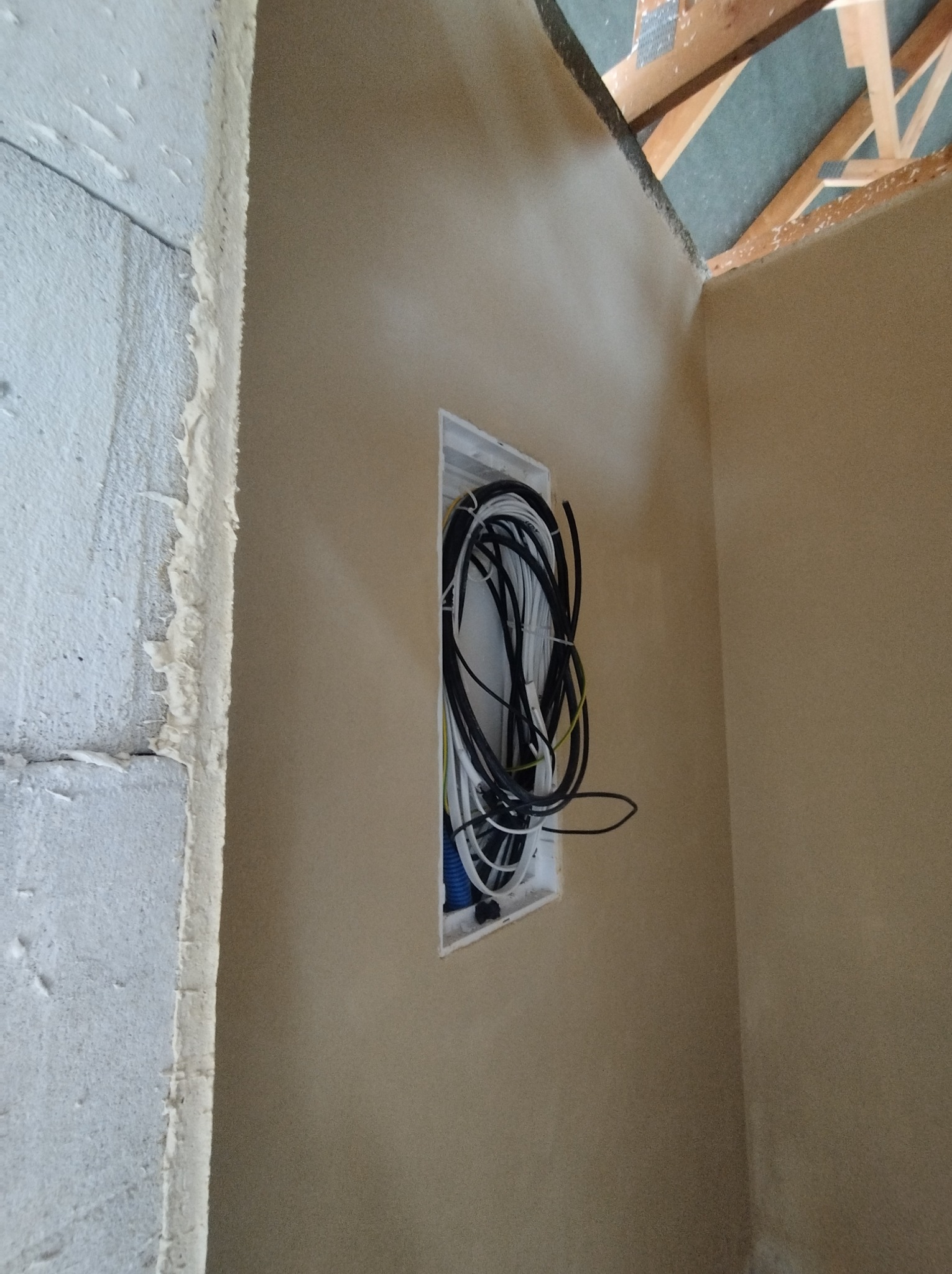 Ściana po nałożeniu gładzi w trakcie prac wykończeniowych, widoczne przewody elektryczne w puszce instalacyjnej i surowy narożnik ściany.