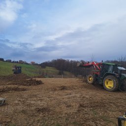 ELKAT - Przygotowanie terenu pod budowę: koparka i traktor z łyżką na błotnistym placu budowy, z widocznym laserowym niwelatorem i odłożoną łyżką koparki w tle.