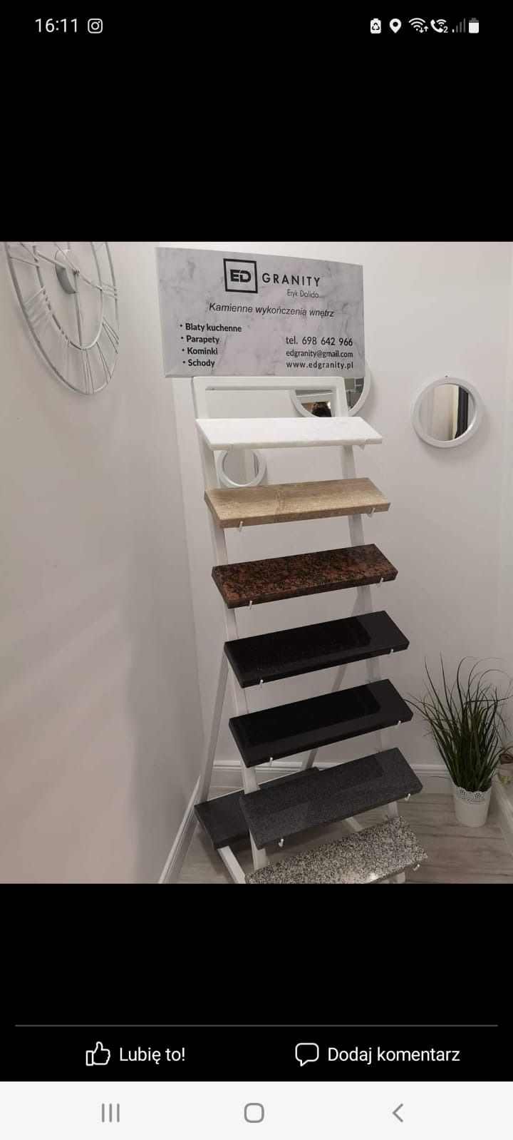 Ekspozycja próbek kamiennych blatów, parapetów i schodów na białym stojaku drabinkowym w minimalistycznym wnętrzu z okrągłymi lustrami i dekoracyjnym zegarem.