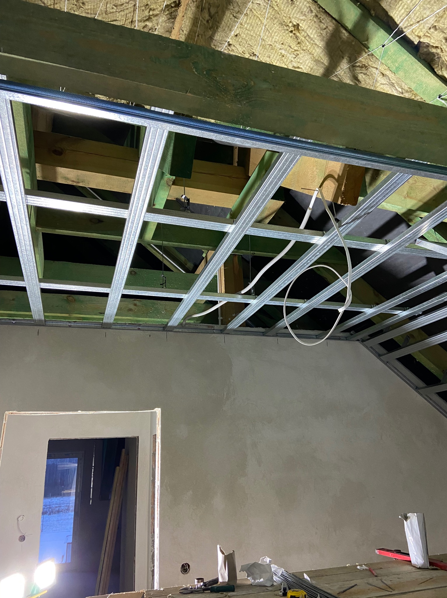 Montaż metalowej konstrukcji sufitu podwieszanego z płyt karton gips, widoczna izolacja wełną mineralną, częściowo wyszpachlowana ściana i fragment ościeżnicy drzwiowej.
