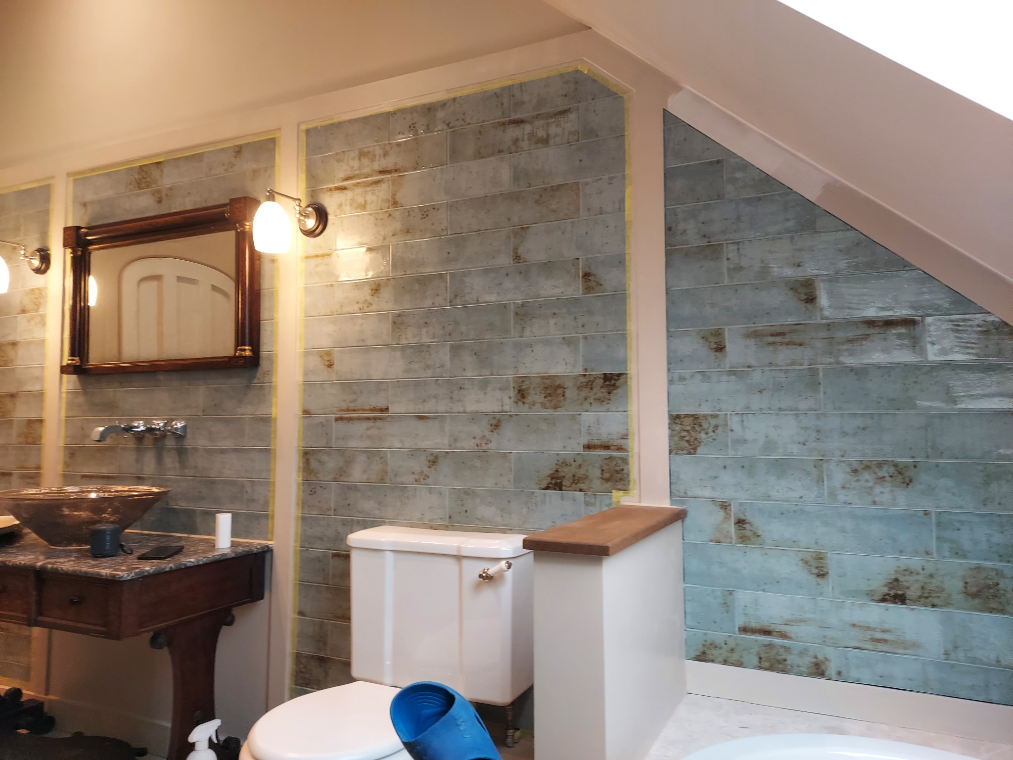 Wykończona łazienka na poddaszu z niebiesko-szarymi, poziomymi płytkami imitującymi drewno, klasyczną umywalką z brązową misą i toaletą z zabudowaną spłuczką.