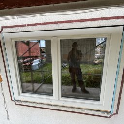 Michał suwisz - Nowe okno PCV z podwójnymi szybami zamontowane w elewacji budynku, widoczne ślady pianki montażowej i odbicie fotografa w szybie.