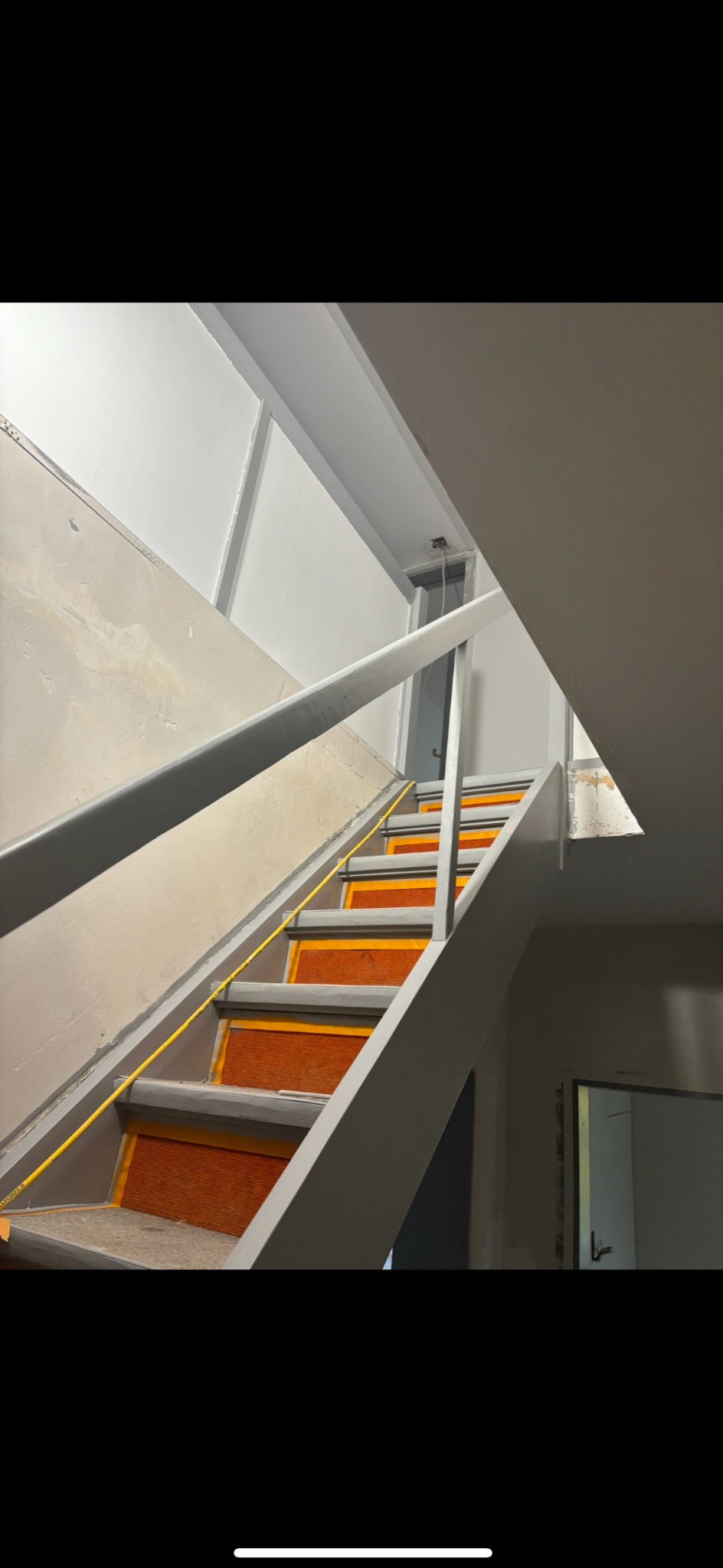 Schody wewnętrzne z pomalowaną na szaro balustradą i stopniami z pomarańczowymi wstawkami antypoślizgowymi, widoczne ślady po malowaniu na ścianie.