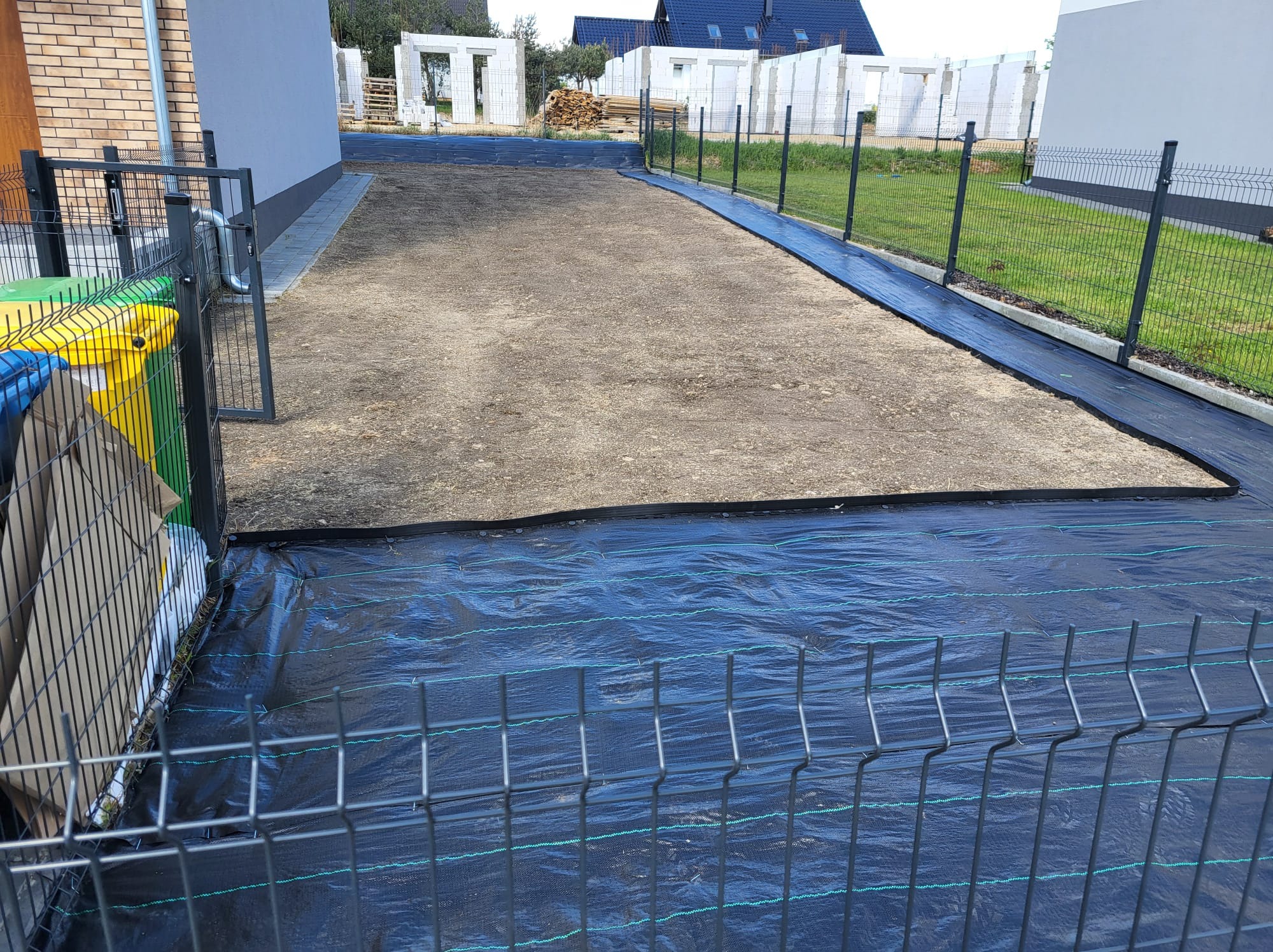 Przygotowany teren pod trawnik w Bolesławcu, z rozłożoną czarną agrowłókniną i wyrównaną ziemią, otoczony ogrodzeniem panelowym.