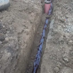 Wykop pod instalacje z rurą kanalizacyjną w brązowej folii ochronnej z napisem 'Kanalizacja' oraz studzienką rewizyjną