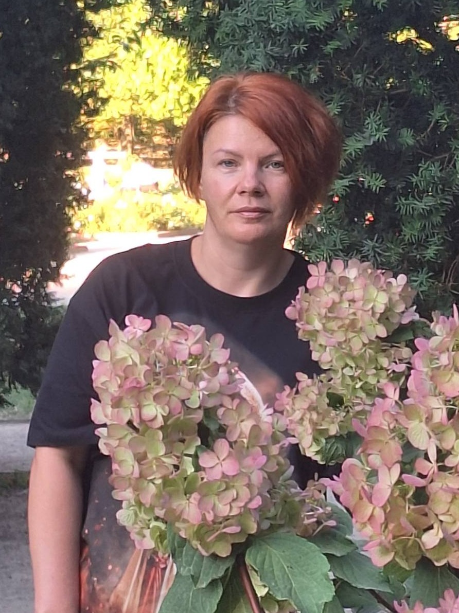 Kobieta z rudymi włosami trzyma bukiet bladoróżowych hortensji na tle zieleni.