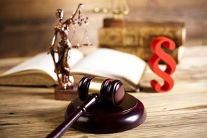 Temida z wagą i mieczem, otwarte księgi, paragraf oraz drewniany młotek sędziowski na drewnianym stole w kancelarii.