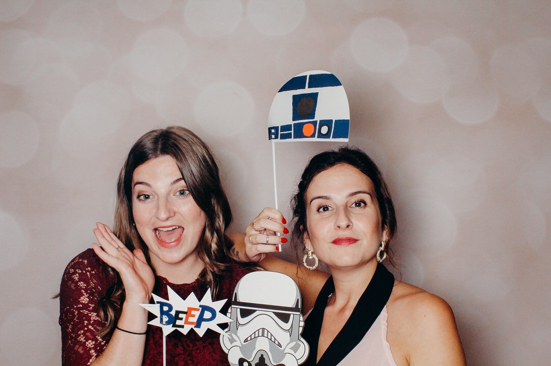 Dwie uśmiechnięte kobiety pozują z rekwizytami Star Wars (maska Stormtroopera i R2-D2) oraz dymkiem z napisem 'BEEP' przed jasnym, rozmytym tłem.