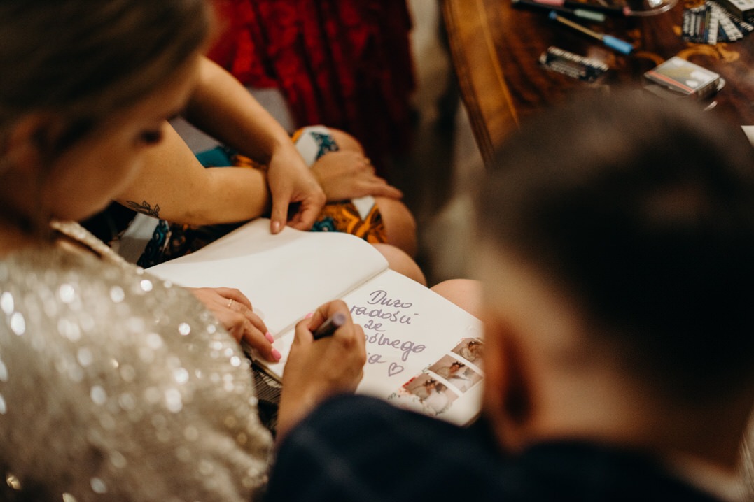 Goście wpisują życzenia do księgi pamiątkowej z naklejonymi zdjęciami z sesji. Zapisane życzenia: 'Dużo radości ze wspólnego życia'.