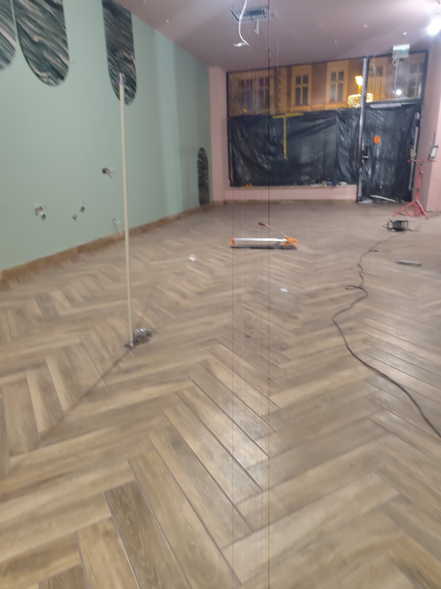 Ukończona podłoga z paneli ułożonych w jodełkę, widoczna w przestronnym wnętrzu z zielonymi ścianami i narzędziami glazurniczymi w tle.