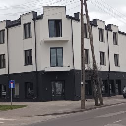 REMWIK Joanna Pęczkowska - Dwukondygnacyjny budynek po renowacji z białą elewacją i ciemnoszarym dołem, widoczny z ulicy w pochmurny dzień. Charakterystyczne okna i detale architektoniczne.