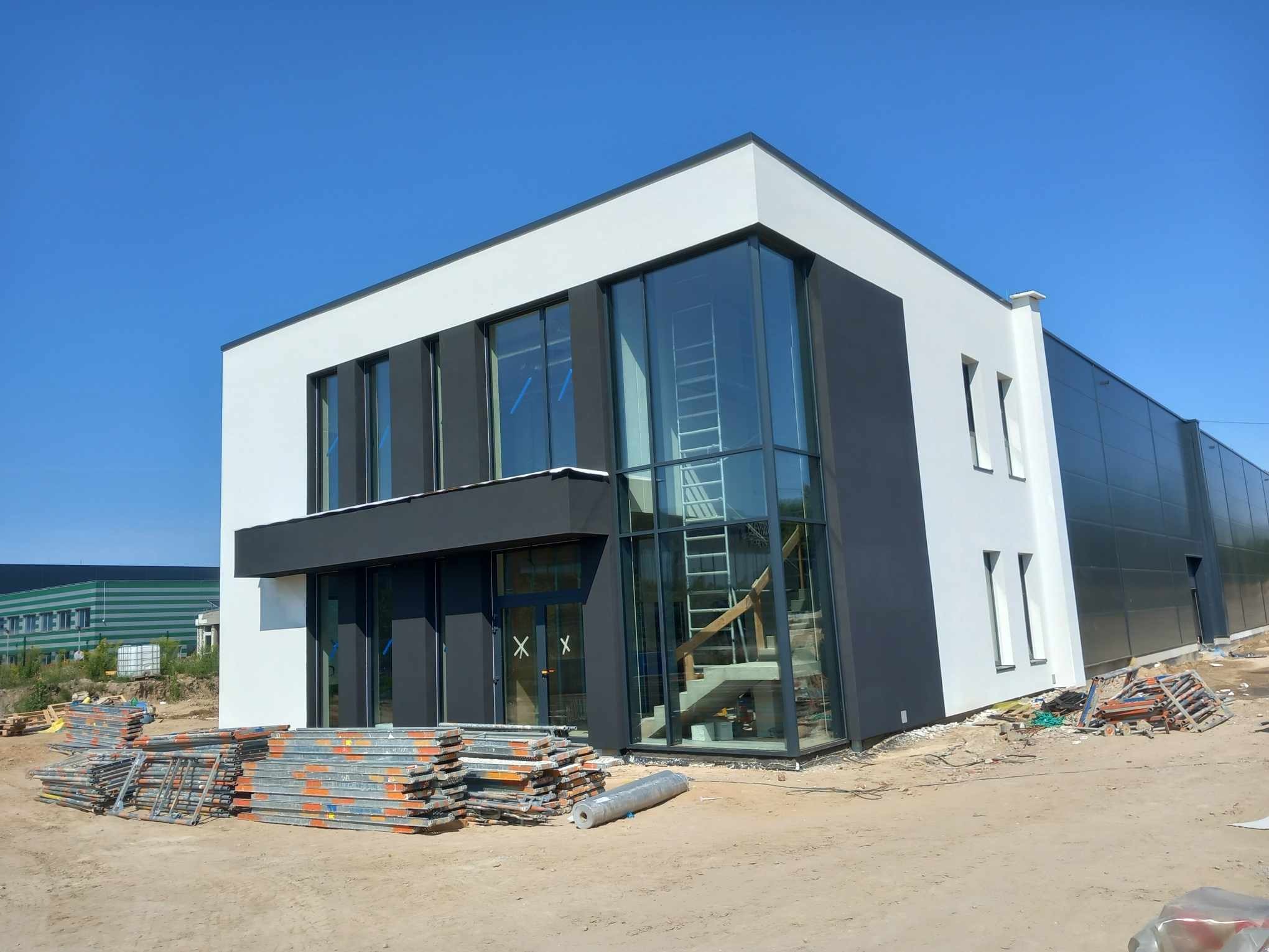 Nowoczesny budynek biurowy w Piotrków Trybunalski po remoncie elewacji, z widocznymi rusztowaniami i elementami wykończeniowymi, w słoneczny dzień.