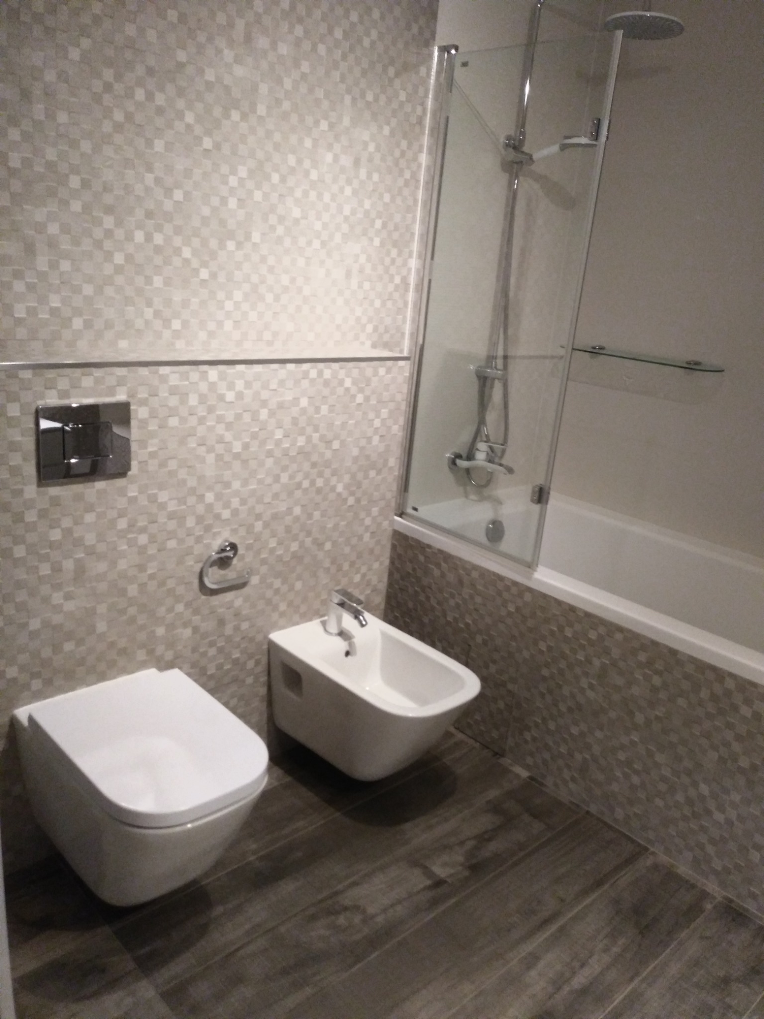 Nowoczesna łazienka z podwieszaną toaletą i bidetem, wykończona mozaiką w odcieniach szarości i kabiną prysznicową z deszczownicą.