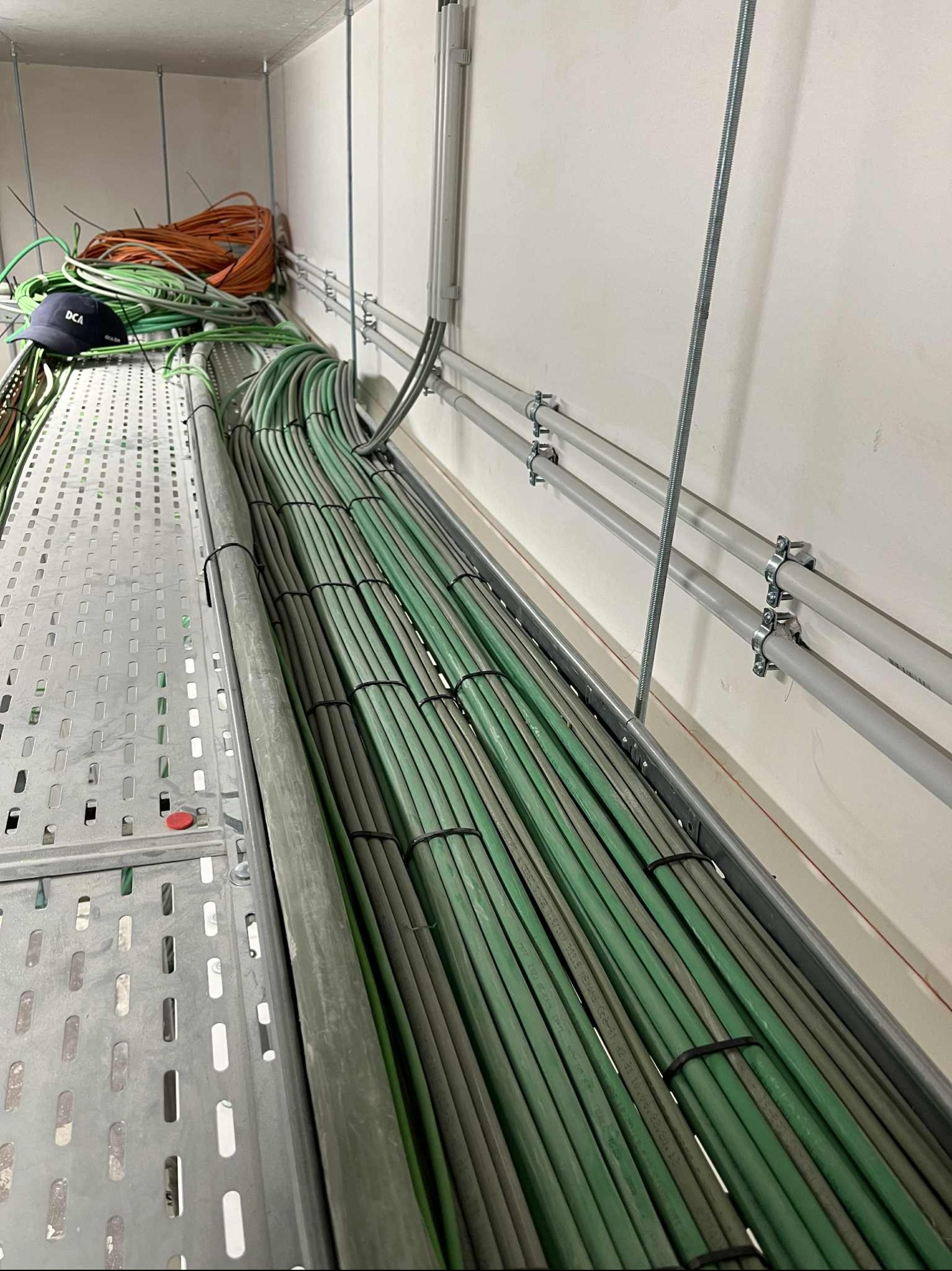 Uporządkowane kable elektryczne w korycie, zabezpieczone czarnymi opaskami, prowadzone wzdłuż ściany z uchwytami. Widoczny fragment rusztowania.
