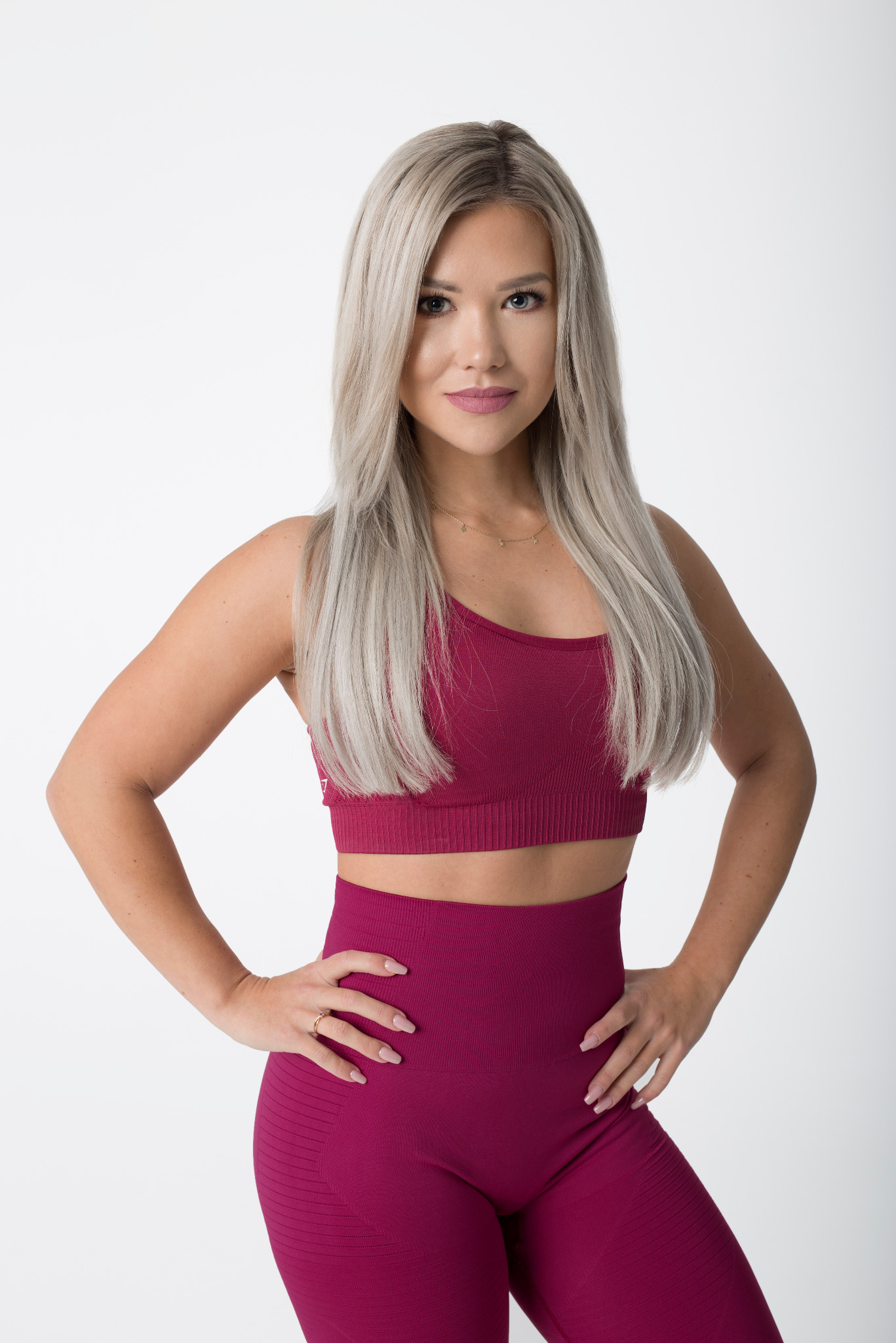 Kobieta w sportowym, bordowym stroju z rękami na biodrach, prezentująca sylwetkę na jasnym tle.