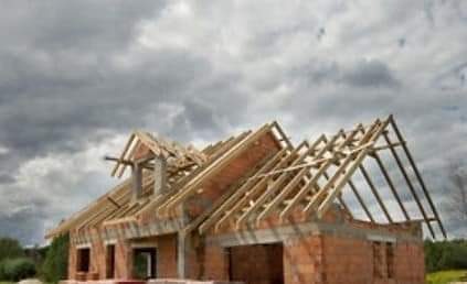 Surowy stan domu z czerwonej cegły z widoczną konstrukcją drewnianą dachu na tle pochmurnego nieba.