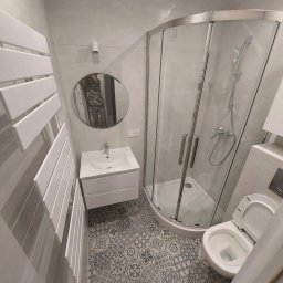 Taras I kompania - Nowoczesna łazienka z kabiną prysznicową narożną, umywalką z szafką, grzejnikiem drabinkowym i toaletą, wykończona szarymi płytkami i dekoracyjną podłogą w stylu vintage.