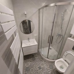 Taras I kompania - Nowoczesna łazienka z kabiną prysznicową, umywalką z szafką, grzejnikiem drabinkowym i toaletą, wykończona płytkami podłogowymi w stylu patchwork.