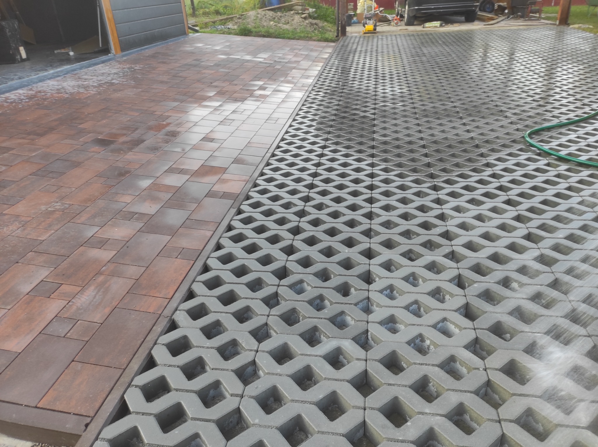 Ułożona kostka brukowa w dwóch wzorach: tradycyjna kostka w odcieniach brązu i ażurowa kostka trawnikowa w kolorze szarym, oddzielone listwą, na podjeździe przed garażem.