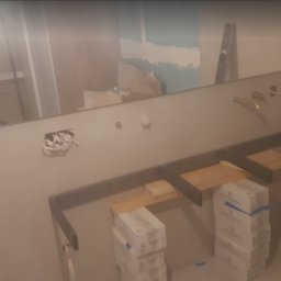 EKODOM REMONTY-WYKOŃCZENIA - Łazienka w trakcie prac: przygotowane stelaże pod umywalki, widoczne puszki elektryczne z przewodami, poziomica oparta o ścianę, w lustrze odbicie osoby robiącej zdjęcie.