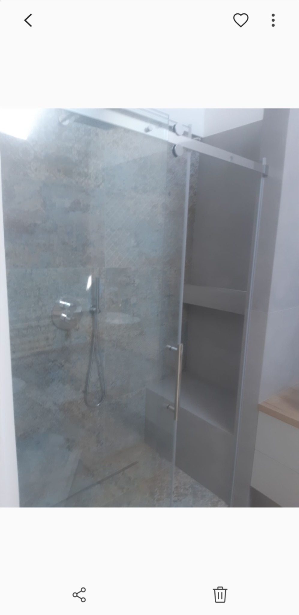 Kabina prysznicowa z przesuwnymi drzwiami ze szkła hartowanego, chromowana armatura, płytki imitujące kamień w odcieniach szarości i beżu, wnęka z półkami po prawej stronie.