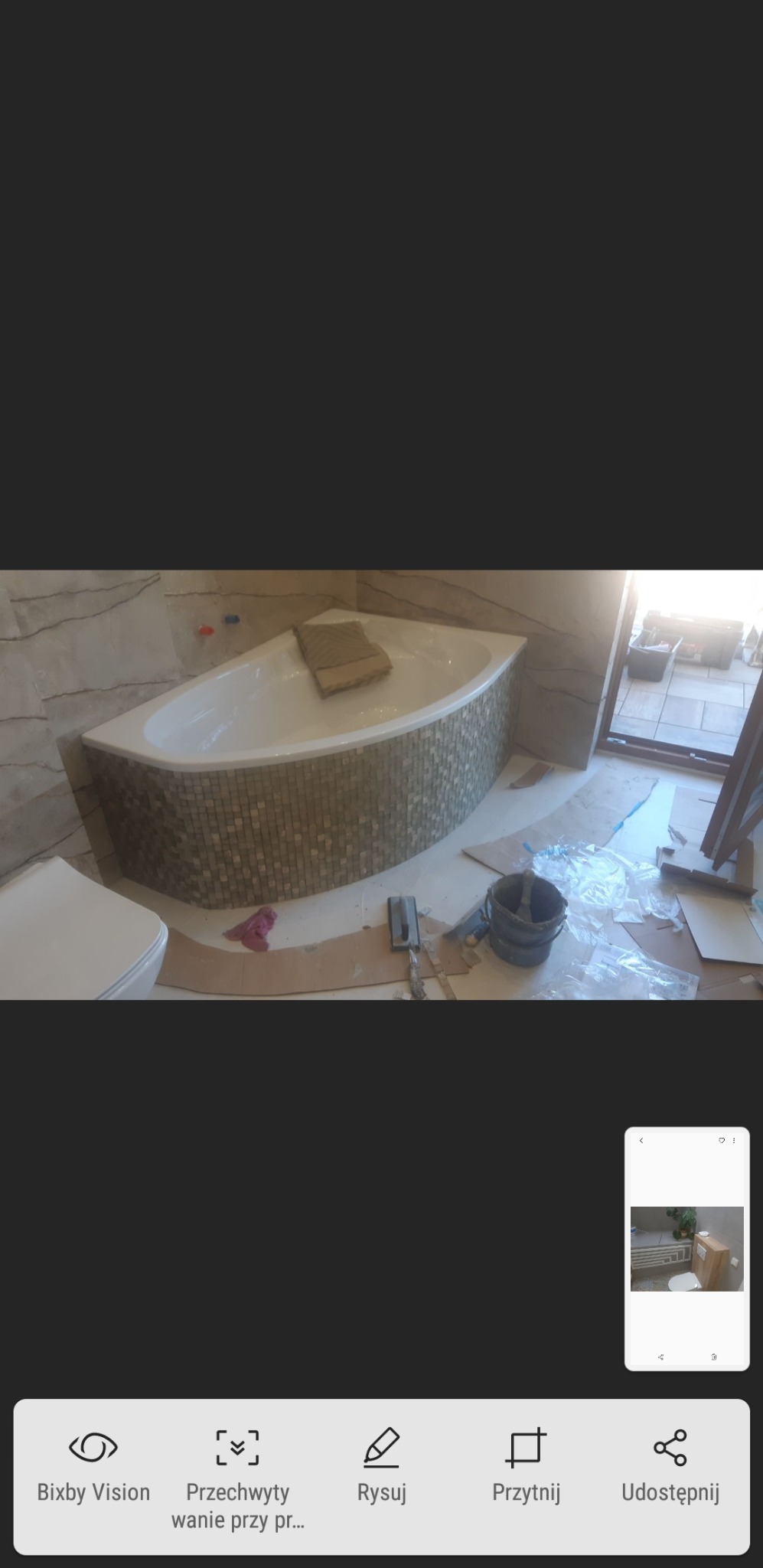 Narożna wanna obudowana mozaiką w trakcie prac wykończeniowych w łazience, widoczne narzędzia i wiadro, częściowo zakryta toaleta.