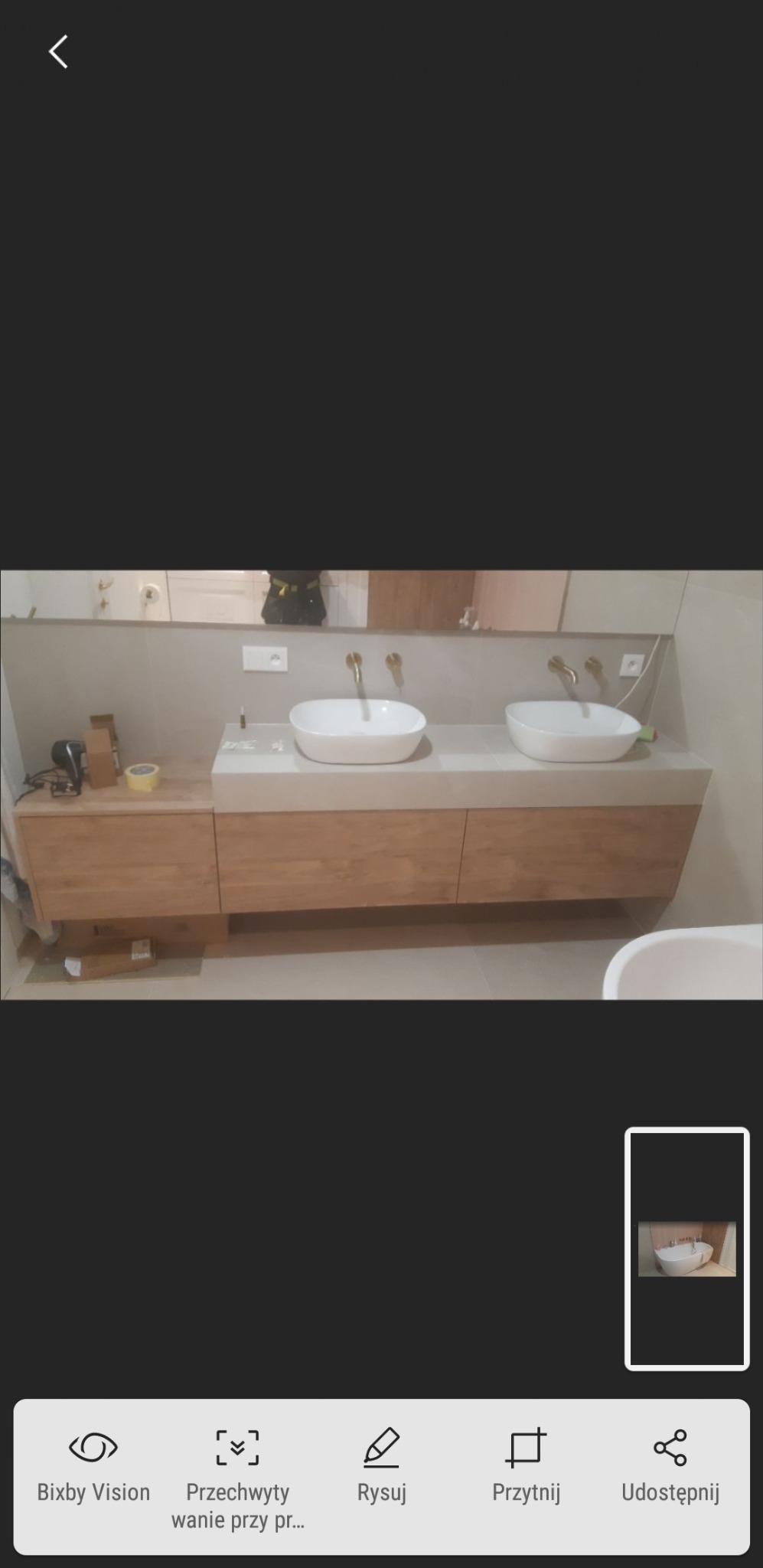 Nowoczesna łazienka z dwoma owalnymi umywalkami nablatowymi, złotymi bateriami i drewnianą szafką pod umywalką. Na blacie widoczne drobne narzędzia i akcesoria.