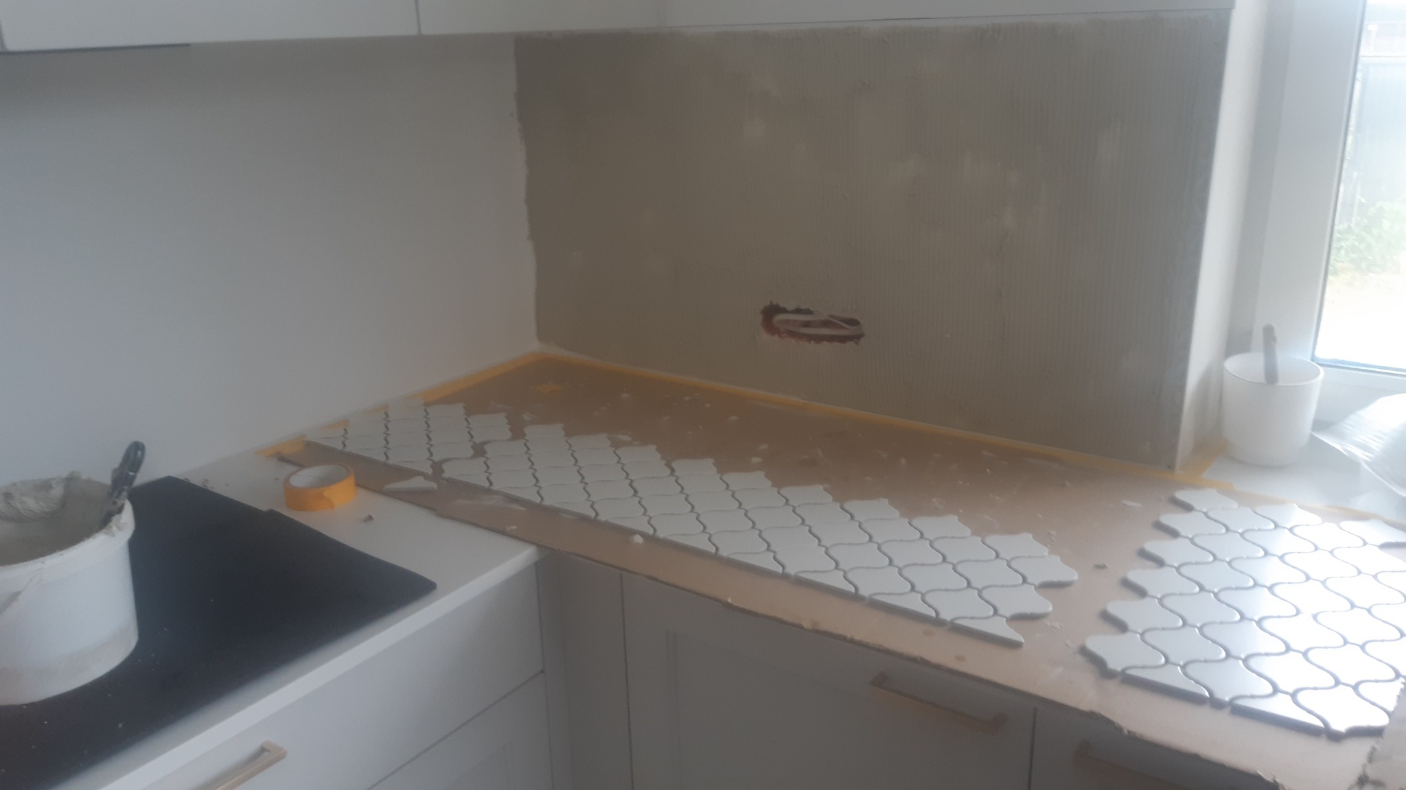 Montaż mozaiki ceramicznej o falistym wzorze na ścianie nad blatem kuchennym w Łodzi, widoczny klej, narzędzia i puszka elektryczna.