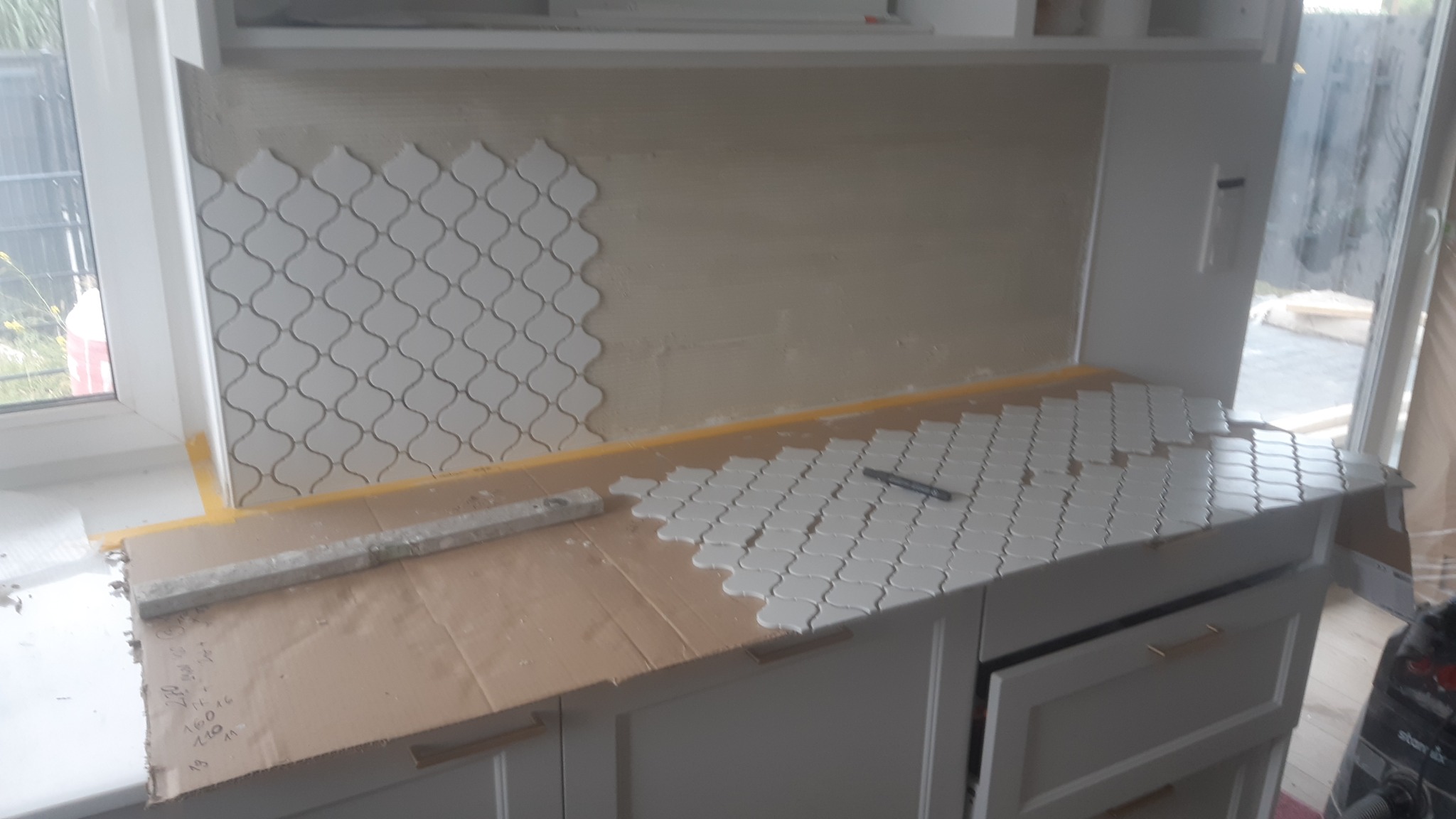 Układanie mozaiki w kształcie koniczyny marokańskiej na ścianie i blacie w kuchni, widoczne narzędzia i etapy pracy.