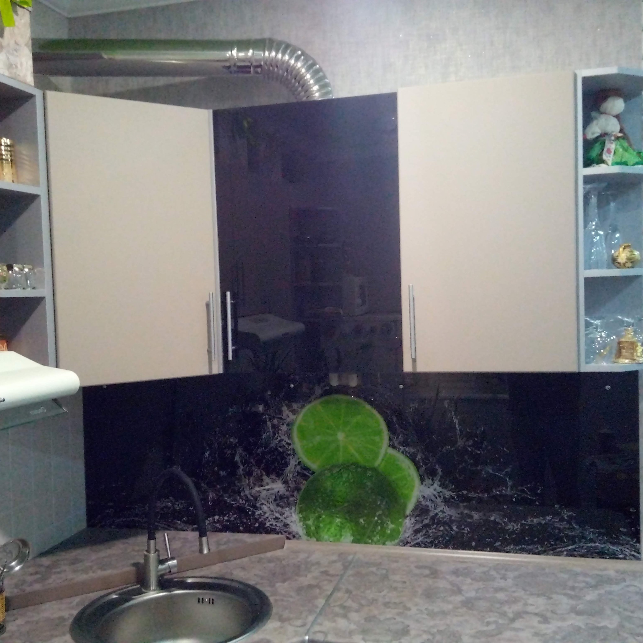 Nowoczesna kuchnia z górnymi szafkami w odcieniach beżu i czarnym panelem nad blatem z motywem limonek, widoczny zlew i bateria.