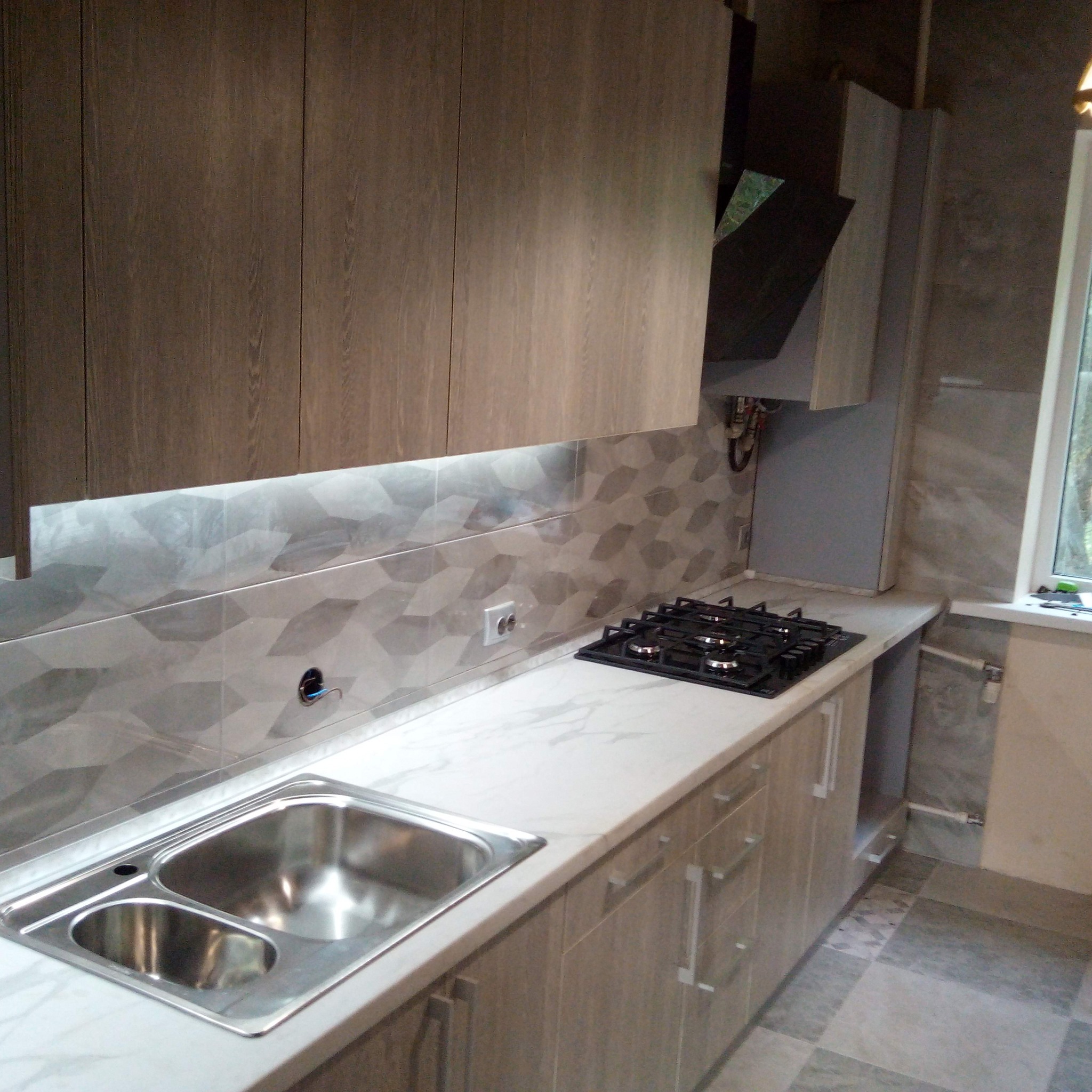 Nowoczesna kuchnia w odcieniach szarości i beżu z drewnopodobnymi frontami szafek, marmurowym blatem, geometrycznymi płytkami na ścianie i oświetleniem LED podszafkowym.