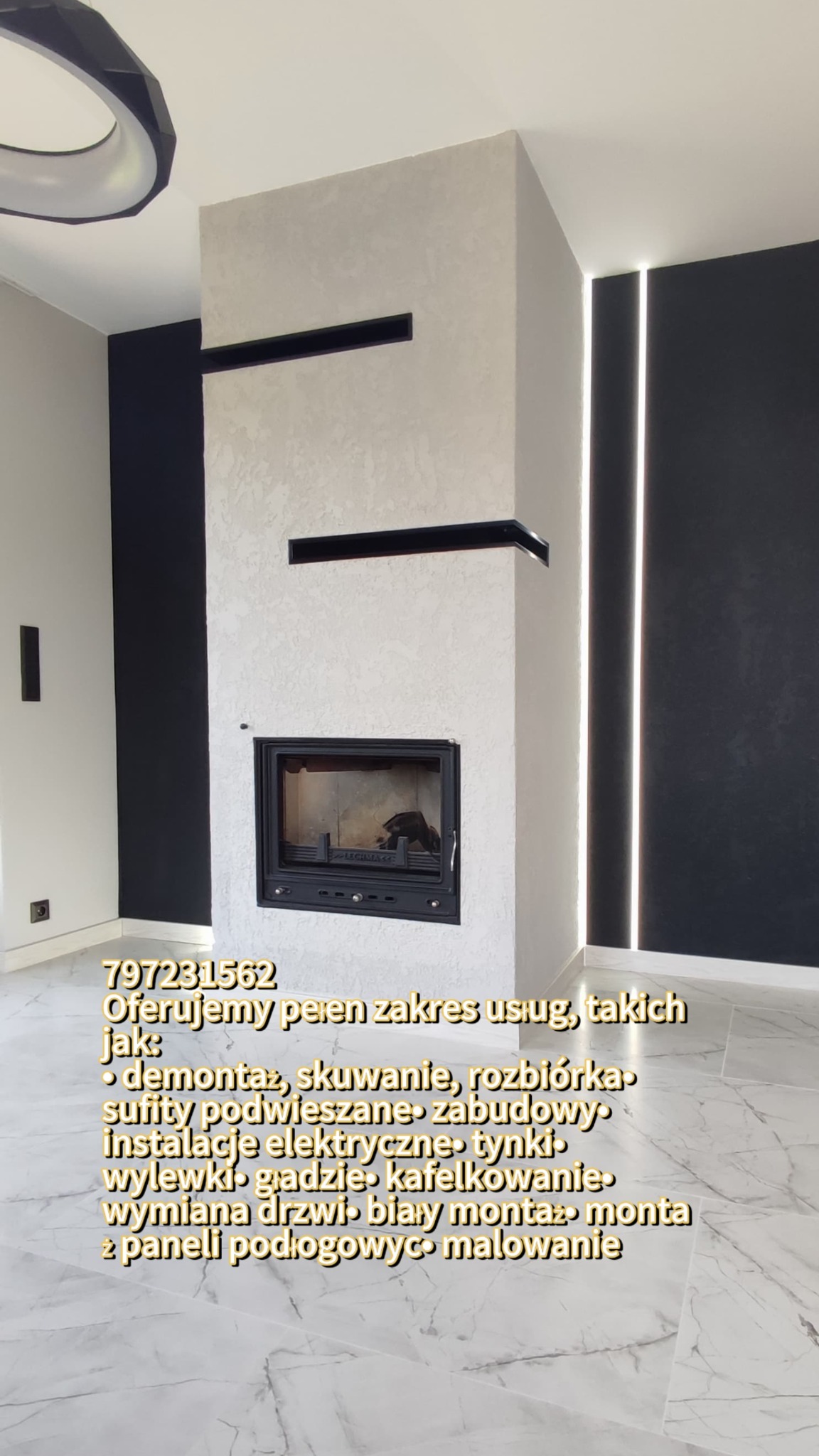 Nowoczesny kominek z obudową w kolorze jasnego betonu architektonicznego, wkomponowany w ścianę z czarnymi panelami, oświetlony pionowymi paskami LED, na marmurowej podłodze.