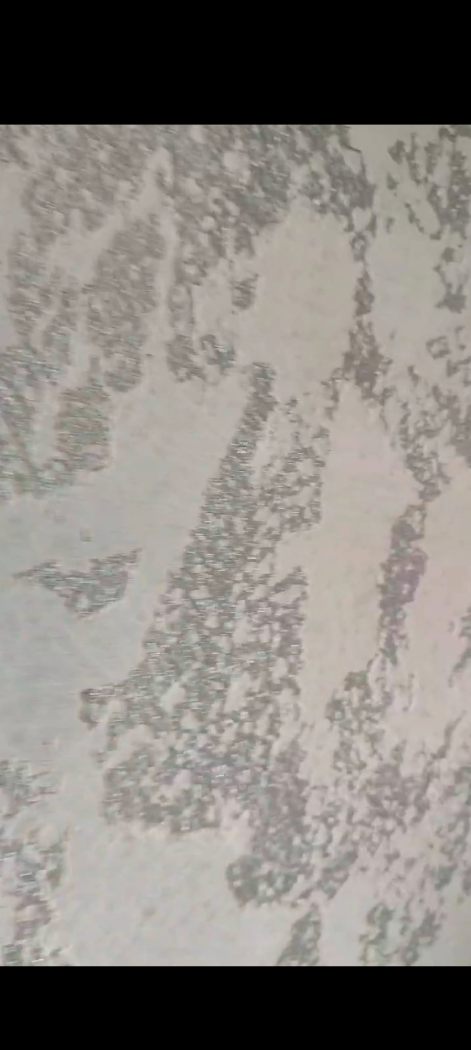 Tekstura ściany z efektem dekoracyjnym w odcieniach szarości i bieli, imitująca naturalny kamień lub beton, z widoczną nieregularną strukturą i subtelnym połyskiem.