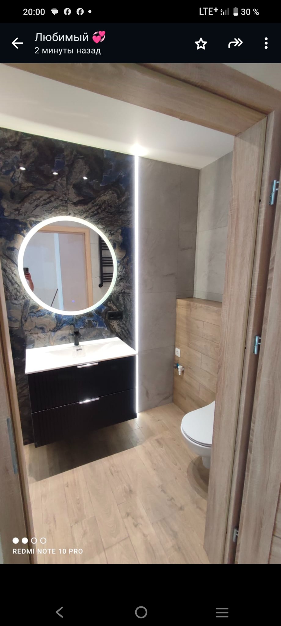 Nowoczesna łazienka w Tychach z okrągłym lustrem podświetlanym LED, czarną szafką pod umywalką i drewnopodobnymi płytkami na podłodze.