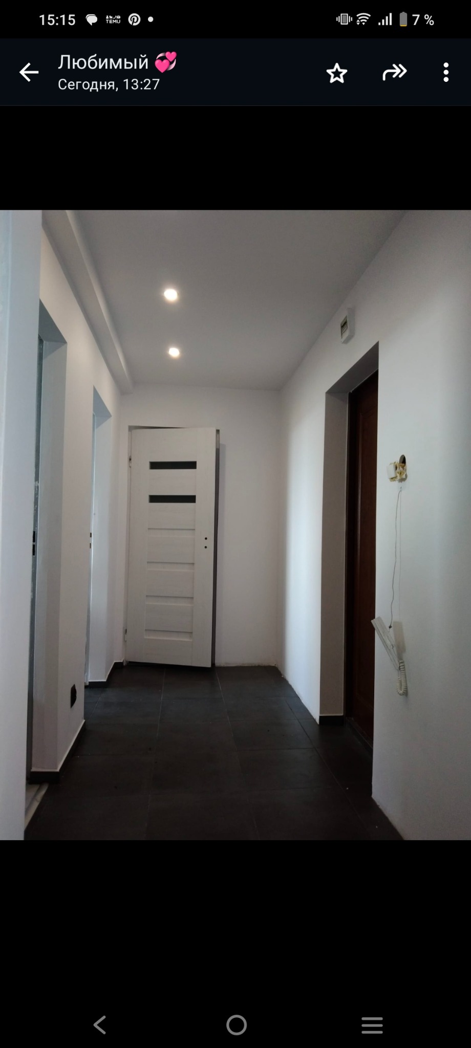 Korytarz po remoncie z ciemną podłogą z płytek, białe ściany, białe drzwi z czarnymi wstawkami i zamontowane oświetlenie punktowe w suficie podwieszanym, widoczny stary telefon na ścianie.