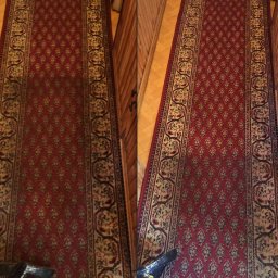 Studio czystości. Pranie dywanów, pranie tapicerki. Czyszczenie posadzek. Ozonowanie Gdynia - Czerwony dywan z wzorem, widoczna różnica w czystości między częścią wypraną a nie wypraną, drewniana podłoga i fragment ściany w tle.