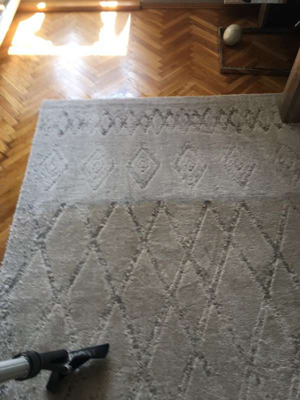 Szary dywan z geometrycznym wzorem czyszczony odkurzaczem na drewnianej podłodze w jodełkę.