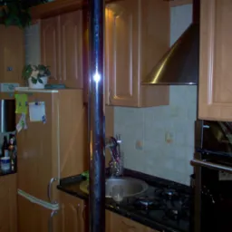 Kuchnia z jasnymi drewnianymi szafkami, czarnym blatem, zlewozmywakiem i płytą gazową; widoczny okap, piekarnik Amica i dekoracje na lodówce.