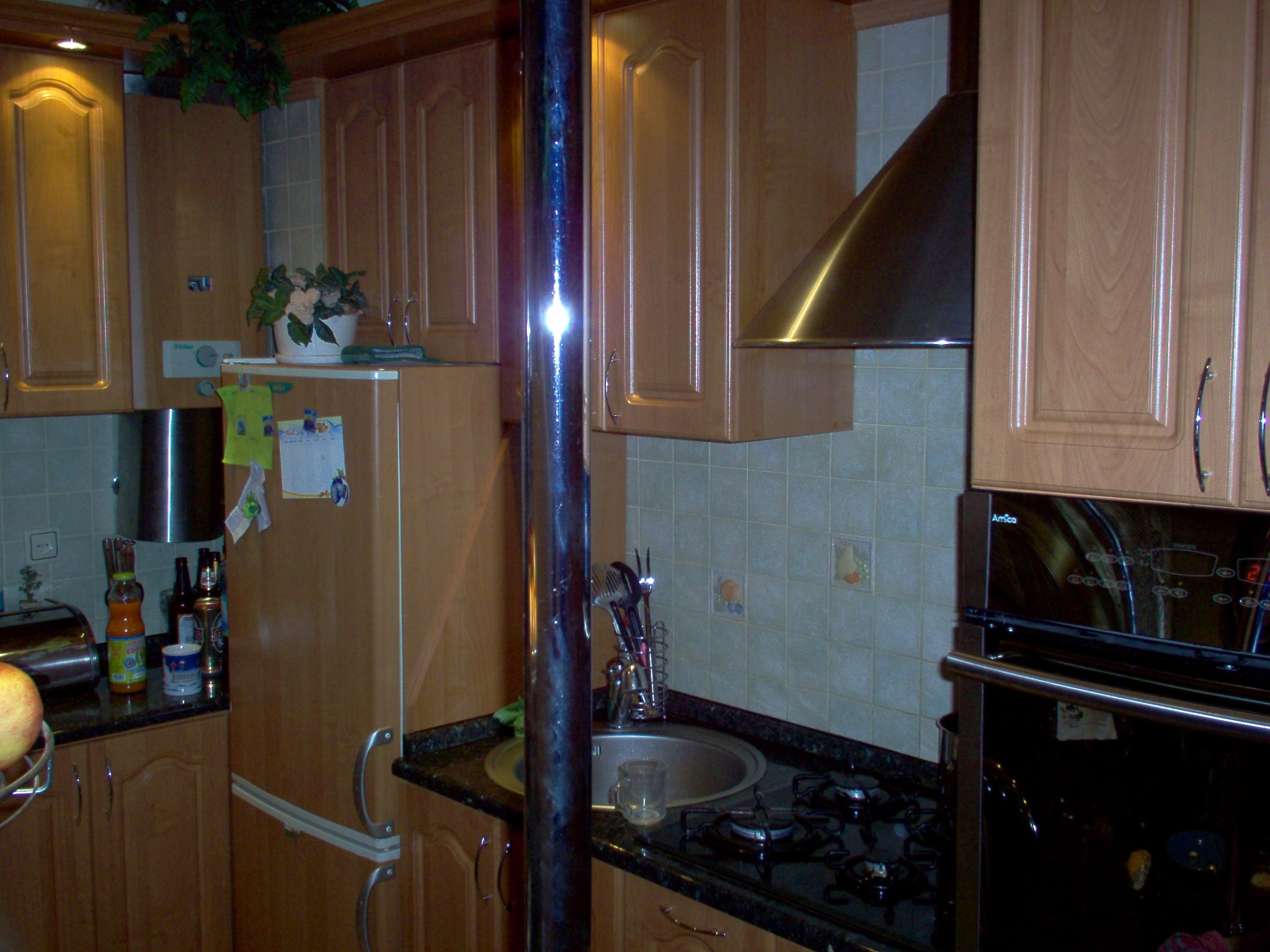 Kuchnia z jasnymi drewnianymi szafkami, czarnym blatem, zlewozmywakiem i płytą gazową; widoczny okap, piekarnik Amica i dekoracje na lodówce.