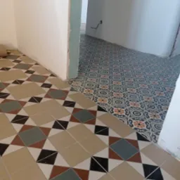 Dwie różne wzorzyste podłogi z płytek ceramicznych w przejściu między pokojami, widoczne niedoskonałości przy łączeniu z ścianą.