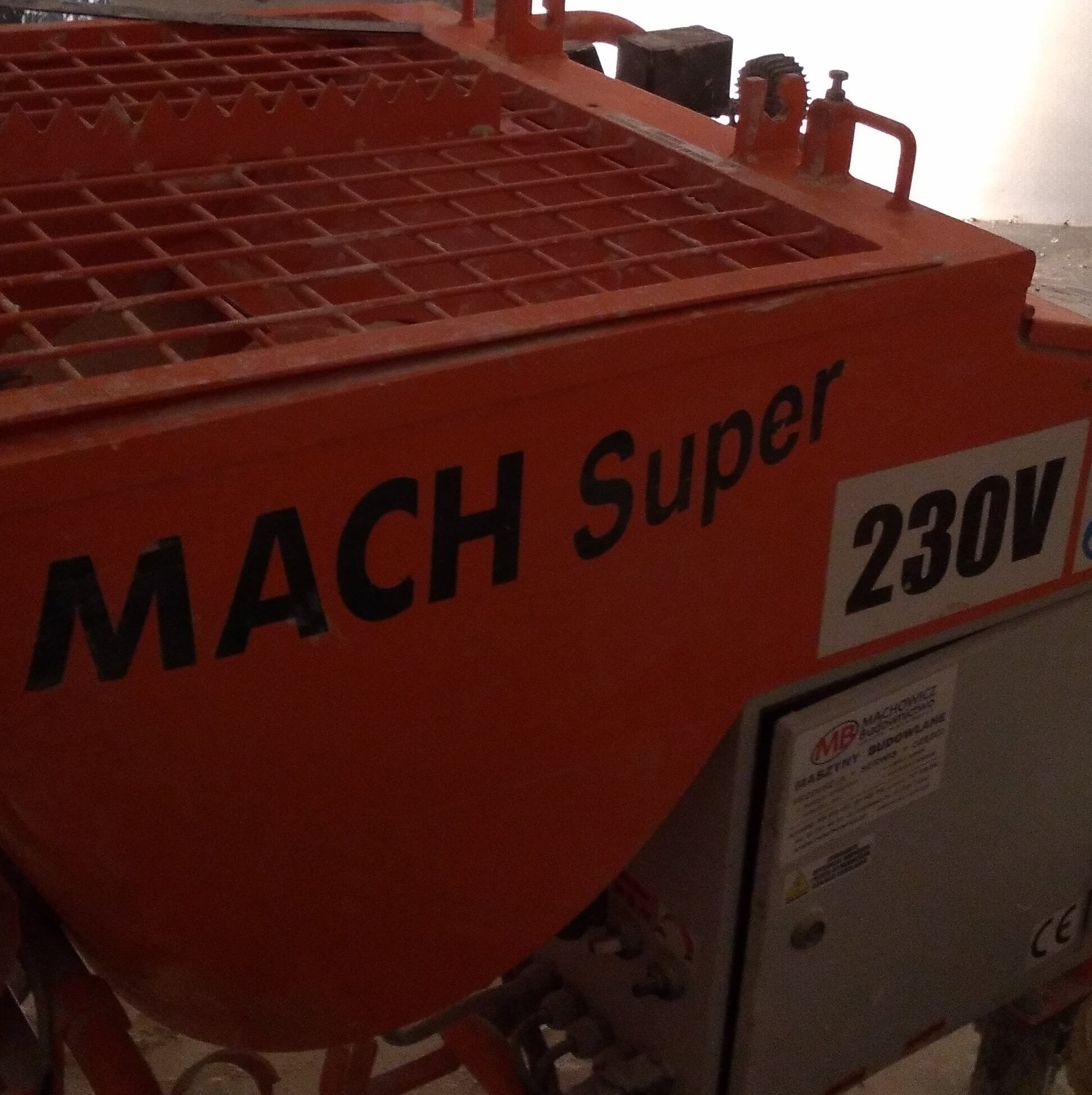 Pomarańczowa maszyna budowlana MACH Super 230V z metalową kratą na górze, widoczna tabliczka informacyjna producenta.