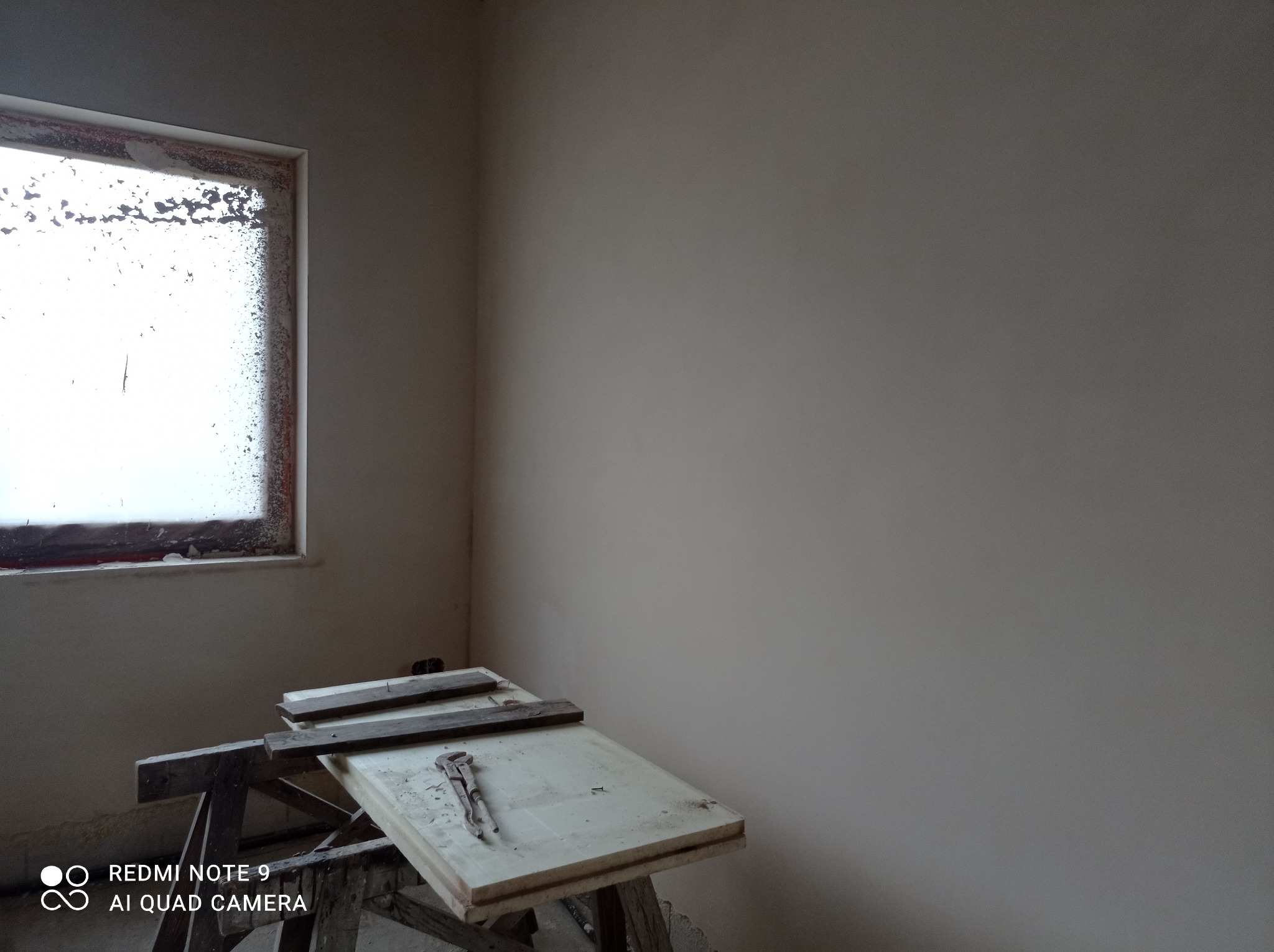 Wnętrze po pracach wykończeniowych: gładkie ściany w neutralnym odcieniu, okno z widocznymi śladami prac, narzędzia na prowizorycznym stole.
