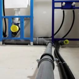 Szare rury kanalizacyjne z obejmami, czarne rury karbowane i niebieskie stelaże podtynkowe do WC podczas montażu w surowym stanie.