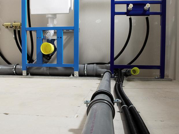 Szare rury kanalizacyjne z obejmami, czarne rury karbowane i niebieskie stelaże podtynkowe do WC podczas montażu w surowym stanie.