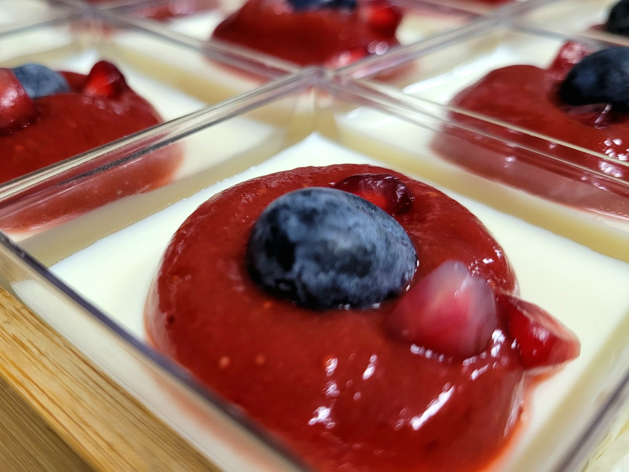 Mini deser w przezroczystym pojemniku z białą bazą, polewą z czerwonych owoców, borówką i ziarnami granatu, przygotowany w Zielonej Górze.