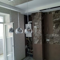 Super - Nowoczesne, szklane lampy wiszące nad balkonem z otwartymi drzwiami, marmurowa okładzina ściany i widoczne instalacje grzewcze.