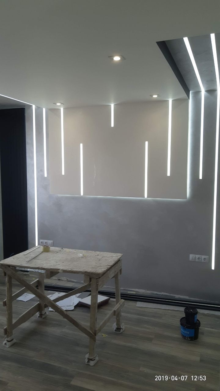 Wnętrze w trakcie wykańczania z dekoracyjnym oświetleniem LED na ścianie, drewniany stołek malarski i puszka z farbą na podłodze.