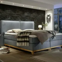 Elegancka sypialnia z łóżkiem kontynentalnym w odcieniach szarości, drewniana rama, kamienna ściana i lampki nocne w stylu skandynawskim.