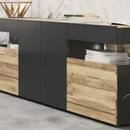 Nowoczesna komoda z czarnymi frontami i elementami z jasnego drewna o wyraźnej strukturze, z otwartymi półkami wypełnionymi książkami, na tle marmurowej ściany.